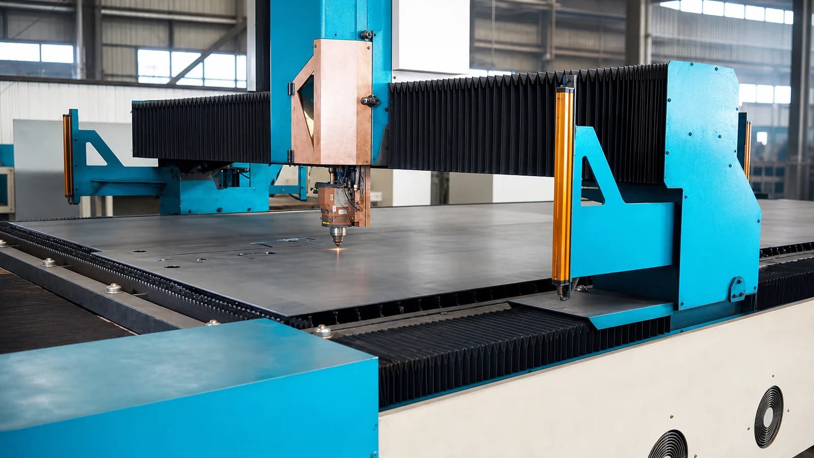 Gantry laser cutting head working across a steel plate on the cutting bed, with cut parts still nested in the sheet